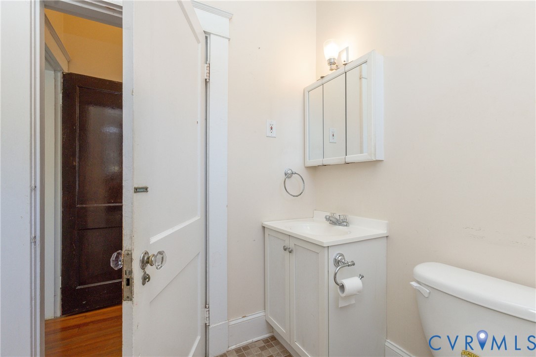 Bathroom featuring a white vanity cabinet with an integrated sink, tri-fold medicine cabinet, wall-mounted light fixture, and classic glass door hardware