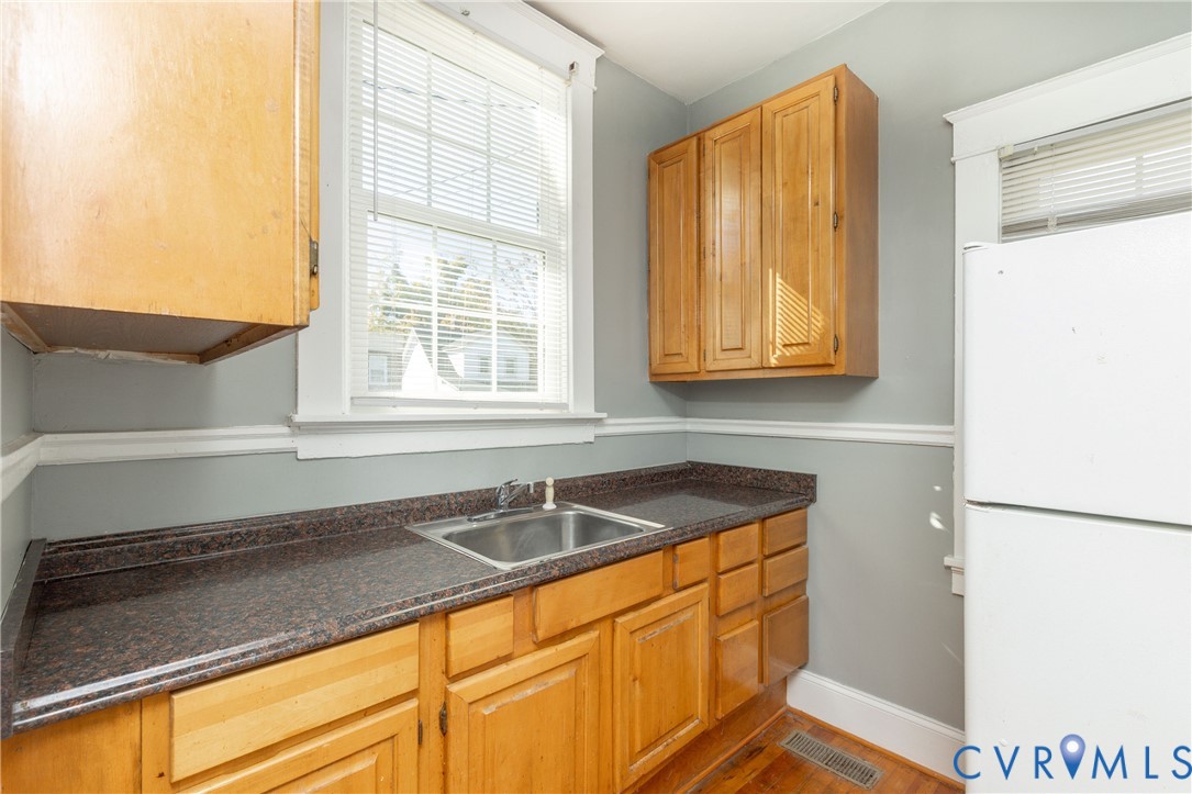 Kitchen featuring natural wood cabinetry, dark stone-finish countertops, stainless steel sink with metal faucet, and windowed walls