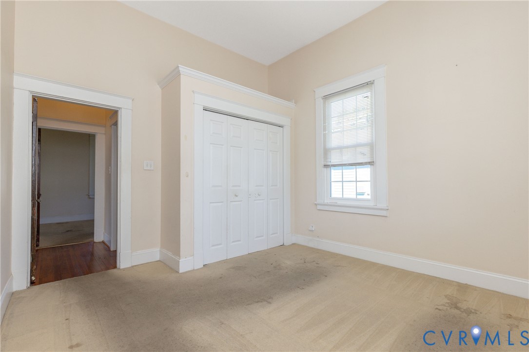 Interior space featuring white-paneled bi-fold closet doors, detailed millwork, neutral wall finishes, and a single-pane window with a horizontal blind