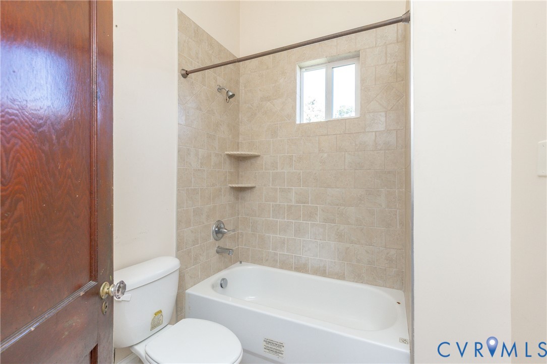Bathroom featuring a white porcelain tub, a surround with square beige wall tiles, built-in corner shelving, and a metal shower rod