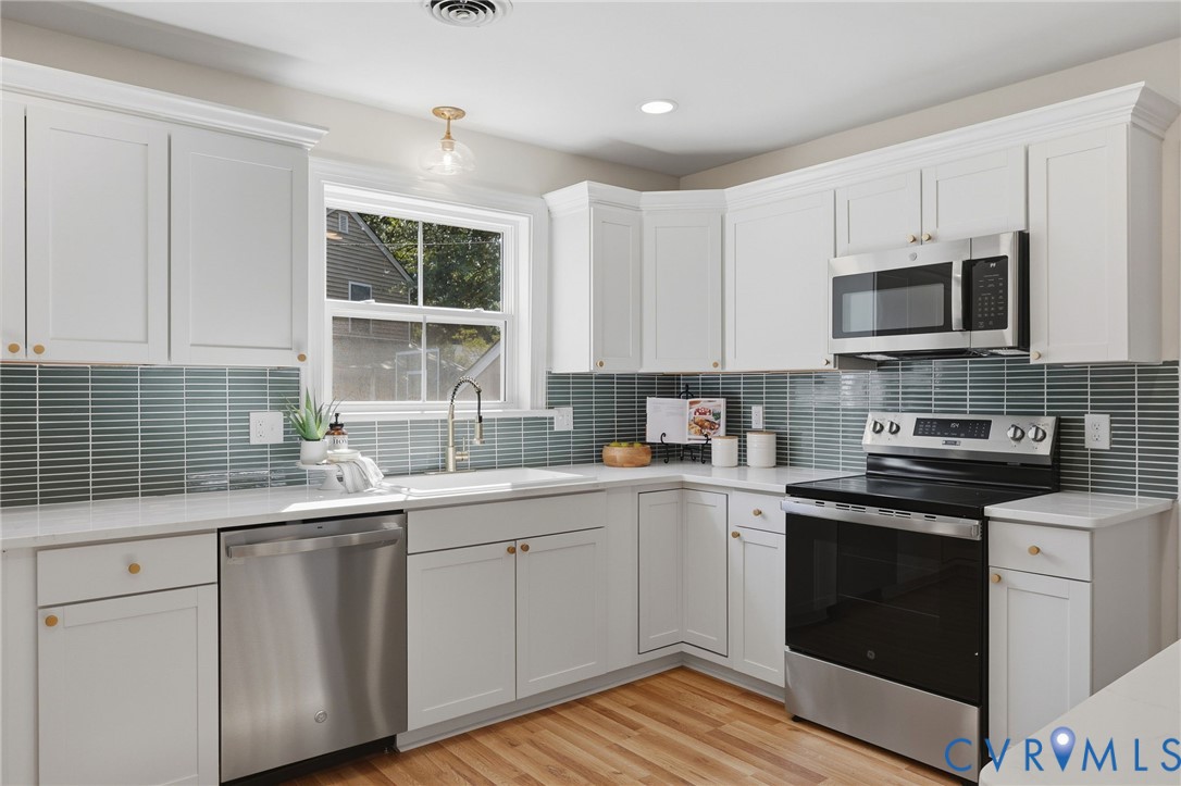 White shaker cabinetry with gold-finish hardware, stainless steel appliances, light-toned countertops, and a full tile backsplash
