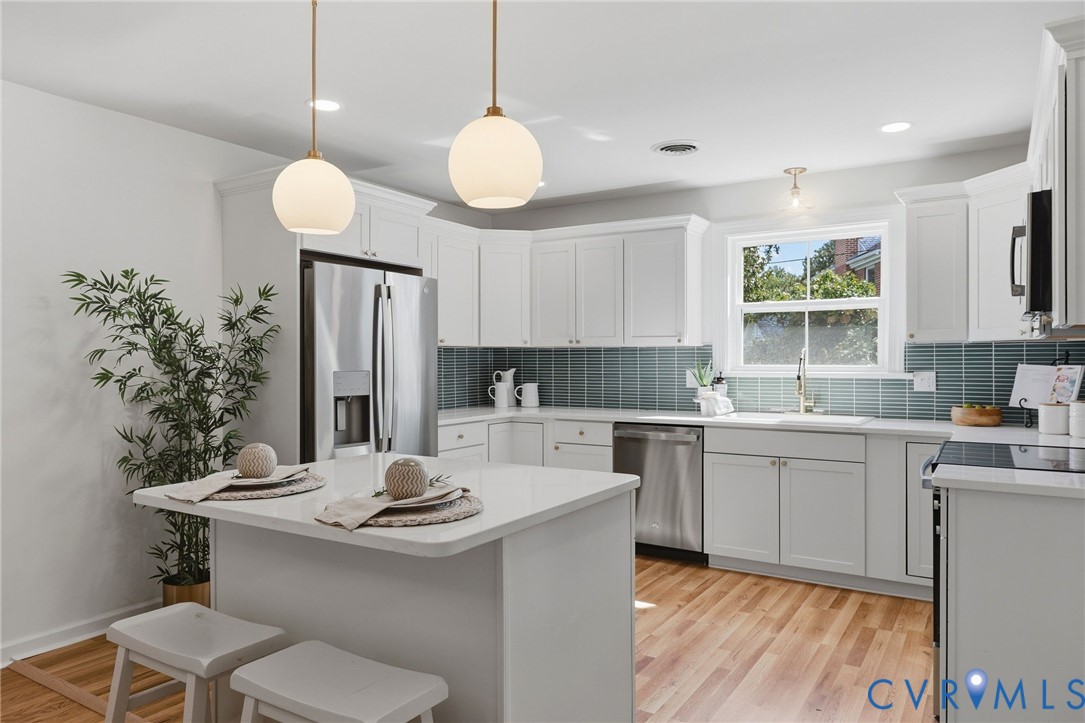 White cabinetry and a waterfall countertop island featuring two pendant lights