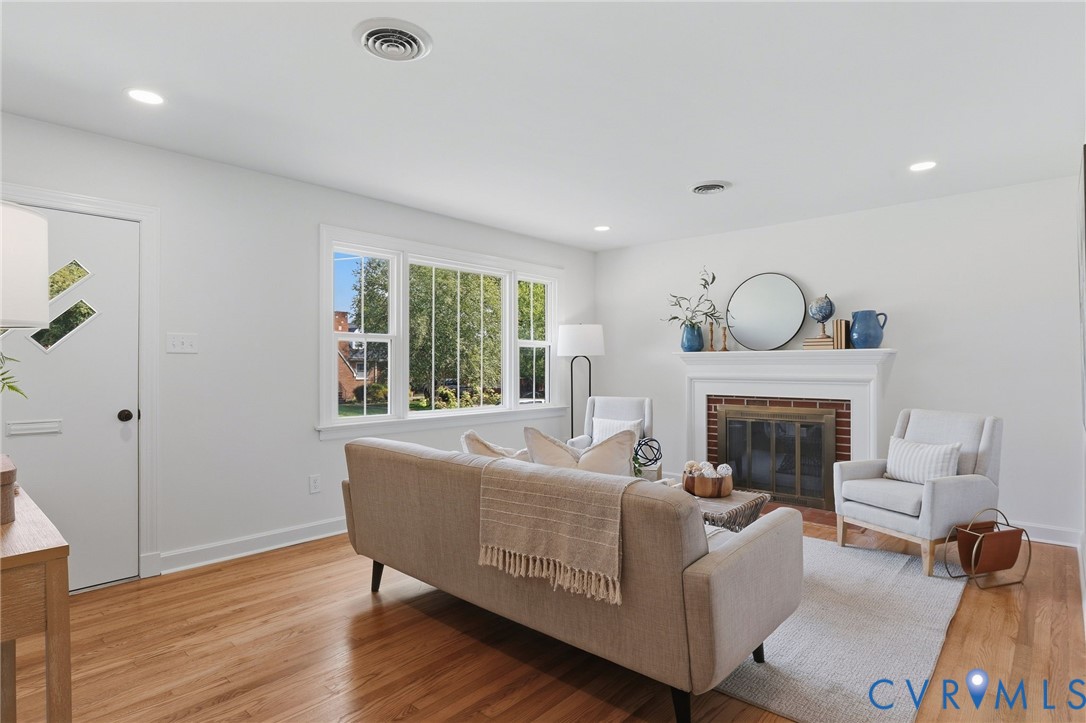 Living area featuring hardwood flooring, a fireplace with a white mantel, recessed lighting, and large windows