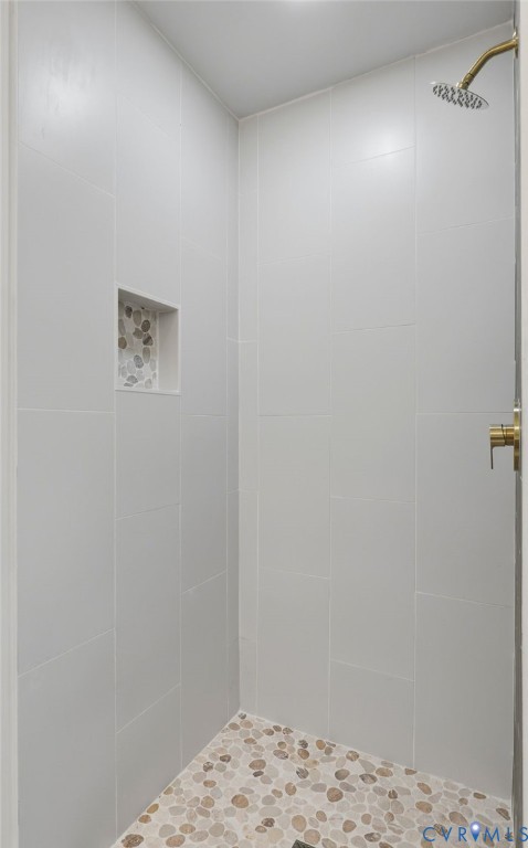 Shower enclosure featuring light-toned wall tiles, a recessed niche with pebble-finish detailing, a pebble-finish floor, and brass-finish fixtures