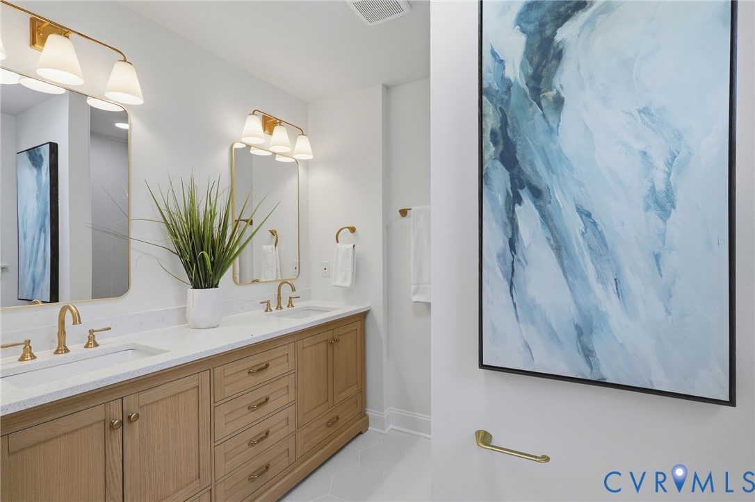 Dual vanity with light wood cabinetry, white countertops, and gold-toned fixtures