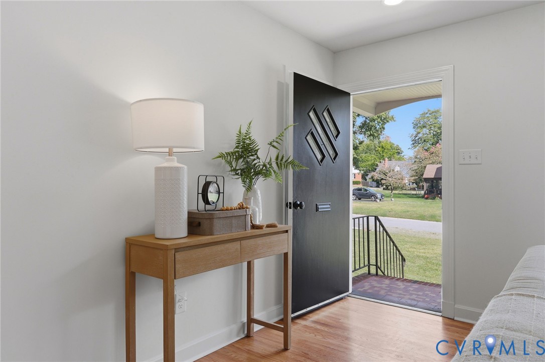 Hardwood-finish flooring, white walls, black front door with decorative paneling, black metal railing, and a clear glass storm door