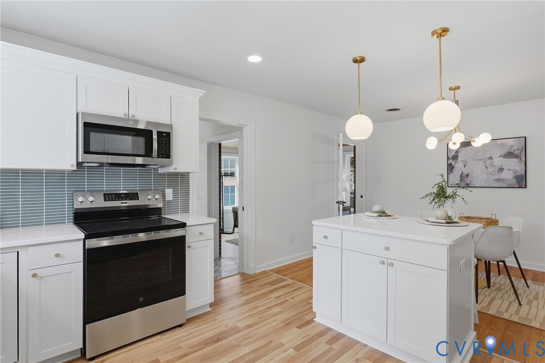 White shaker cabinetry, stainless steel appliances, light wood-finish flooring, white quartz countertops, and a white kitchen island