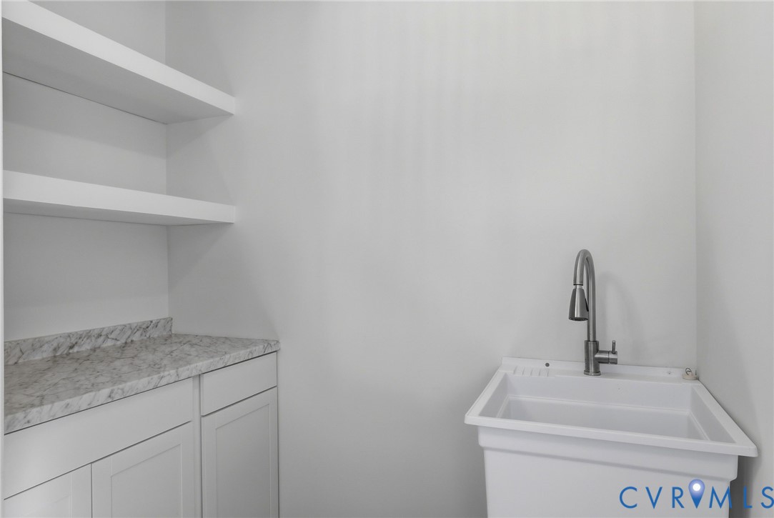 Utility sink with a stainless steel faucet, floating shelves, and white cabinetry with a light-toned countertop