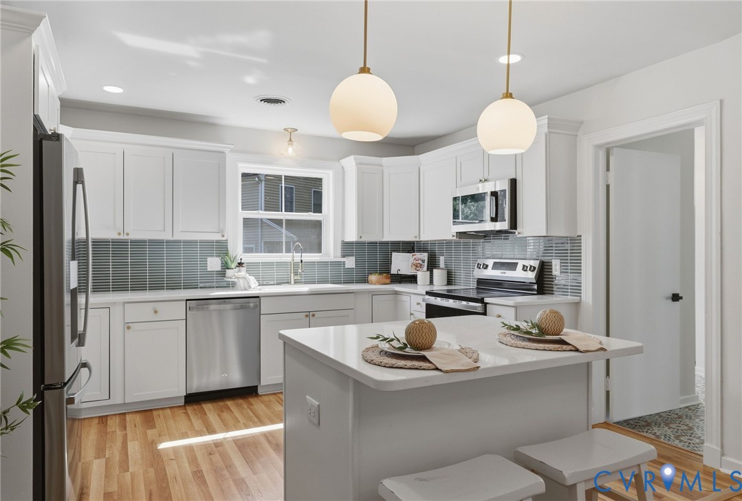 Kitchen featuring white cabinetry, stainless steel appliances, a center island with countertop seating, wood-finish flooring, and pendant lighting