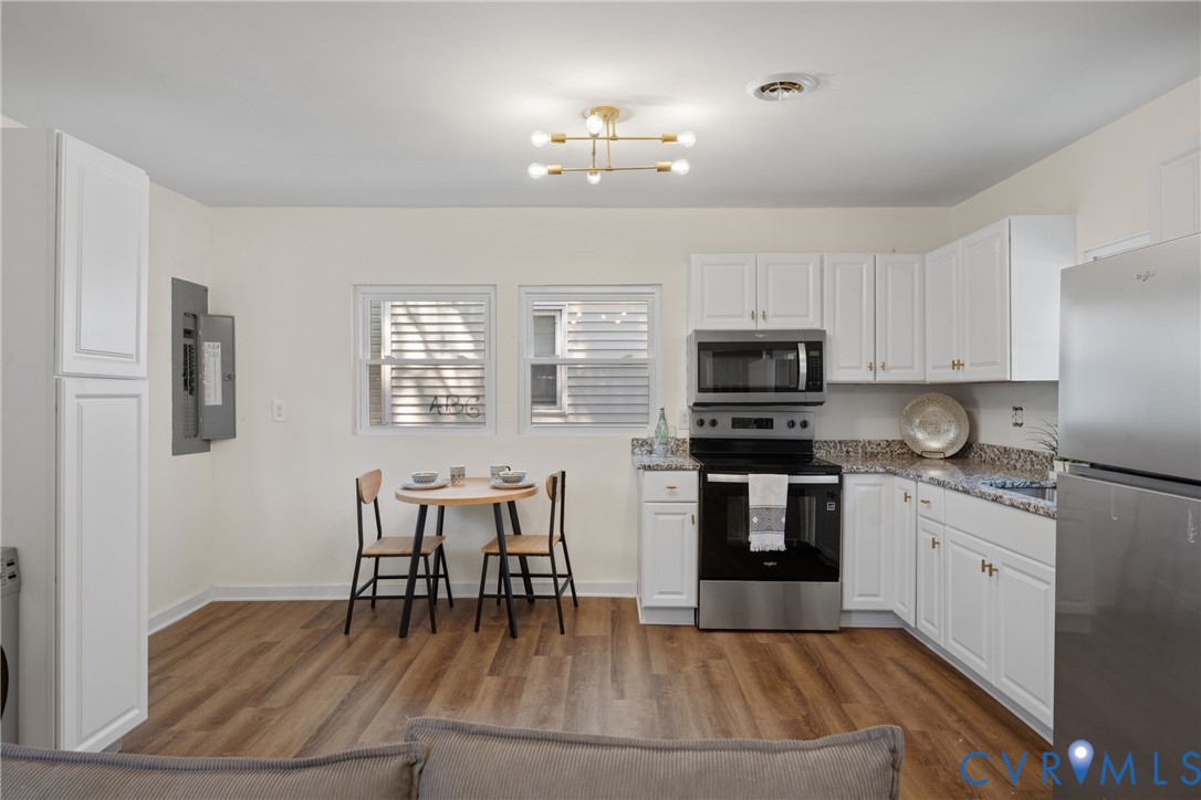 White cabinetry with gold-tone hardware, stainless steel appliances, granite countertops, wood-finish flooring, and a modern ceiling fixture