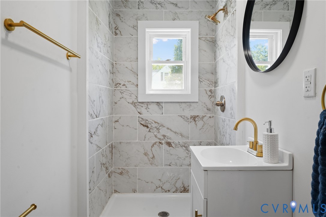 Shower with tile surround, white framed window, and gold-finish fixtures