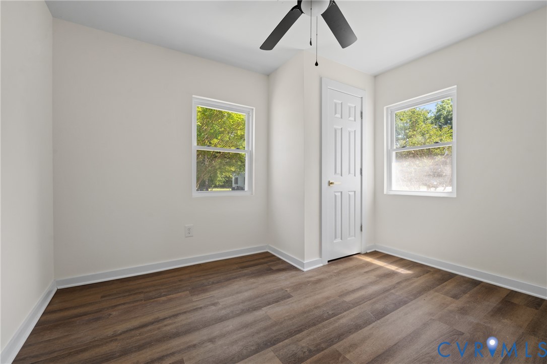 Wood-finish flooring, white walls, two windows with white trim, white paneled door, and a ceiling fan with light fixture