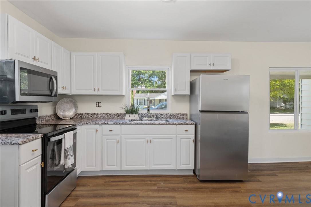 White cabinetry, granite-finish countertops, stainless steel appliances, wood-finish flooring, and a large window