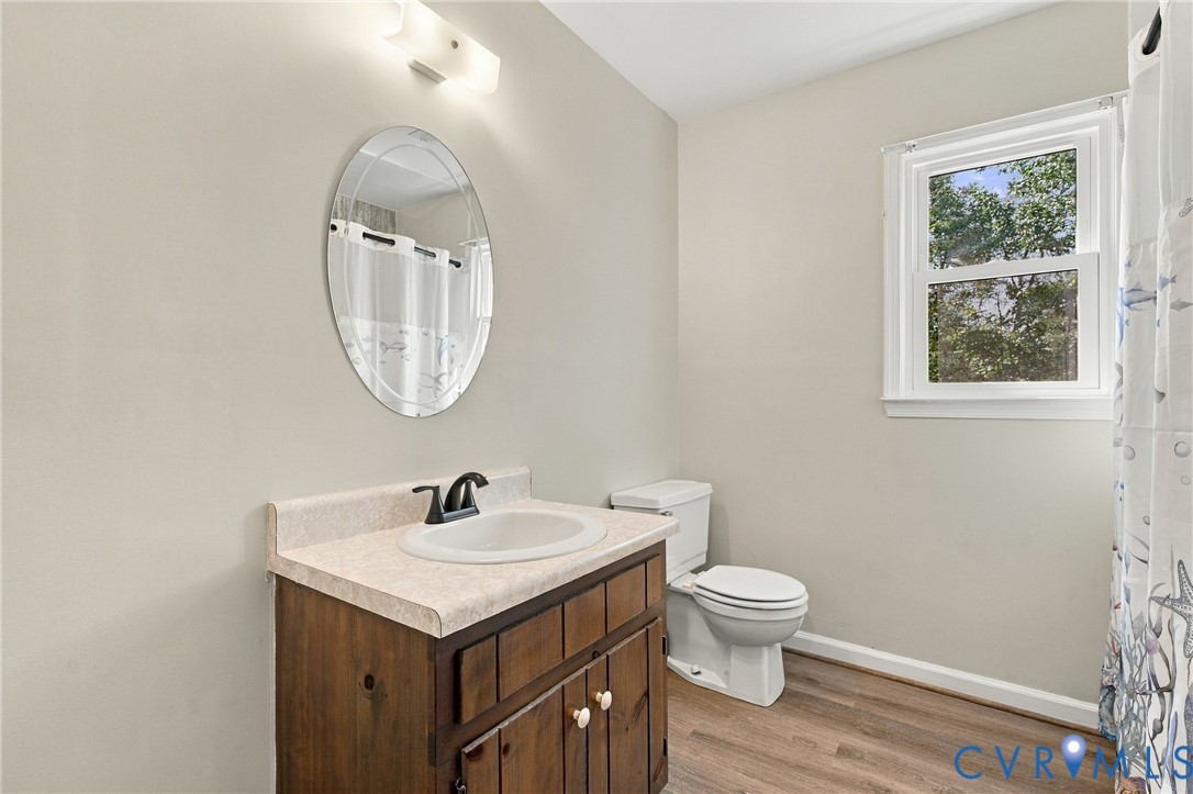 Bathroom featuring wood-finish flooring, a vanity with a stone-composite countertop and integrated sink, a wall-mounted oval mirror, and an exterior window