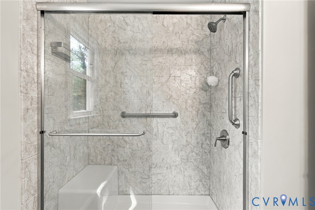 Walk-in shower featuring patterned tile surround, sliding glass doors, a built-in bench seat, and stainless steel hardware