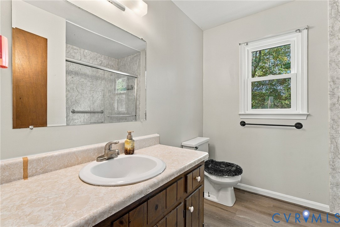 Bathroom featuring a wood-tone vanity, laminate countertop with integrated sink, large wall-mounted mirror, single-hung window, and wood-finish flooring