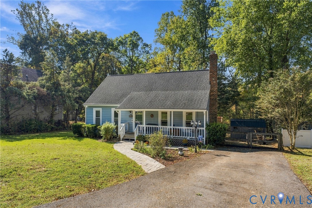Single-story residence featuring blue siding, a covered front porch with white railing, an asphalt driveway, and a masonry chimney