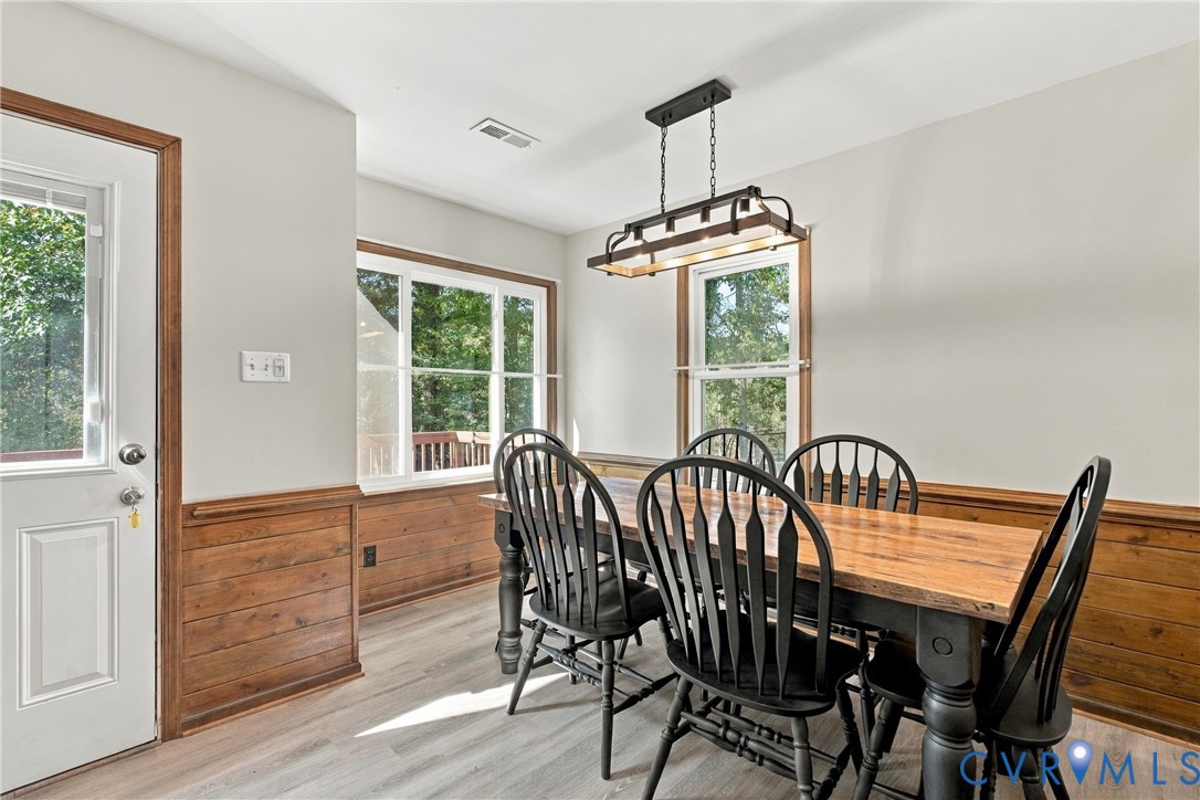 Dining area featuring wood-finish wainscoting, wood-finish flooring, multi-pane windows, and a rectangular multi-light pendant fixture