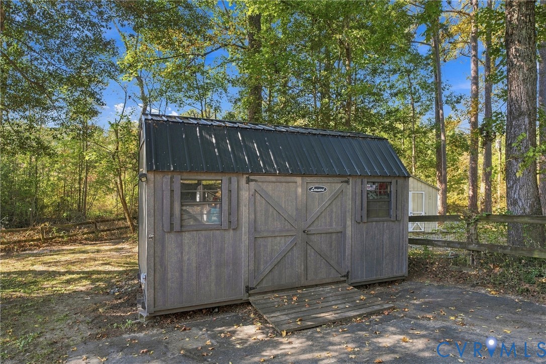 Detached storage building featuring a dark metal gambrel roof, gray vertical wood-textured siding, double-door entry with ramp, and two side windows