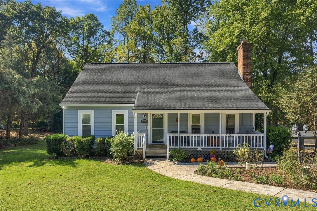Single-story residence featuring light blue horizontal siding, a covered front porch with a white balustrade, a stone-patterned walkway, and an exterior brick chimney Single-story residence featuring light blue horizontal siding, a covered front porch with a white balustrade, a stone-patterned walkway, and an exterior brick chimney