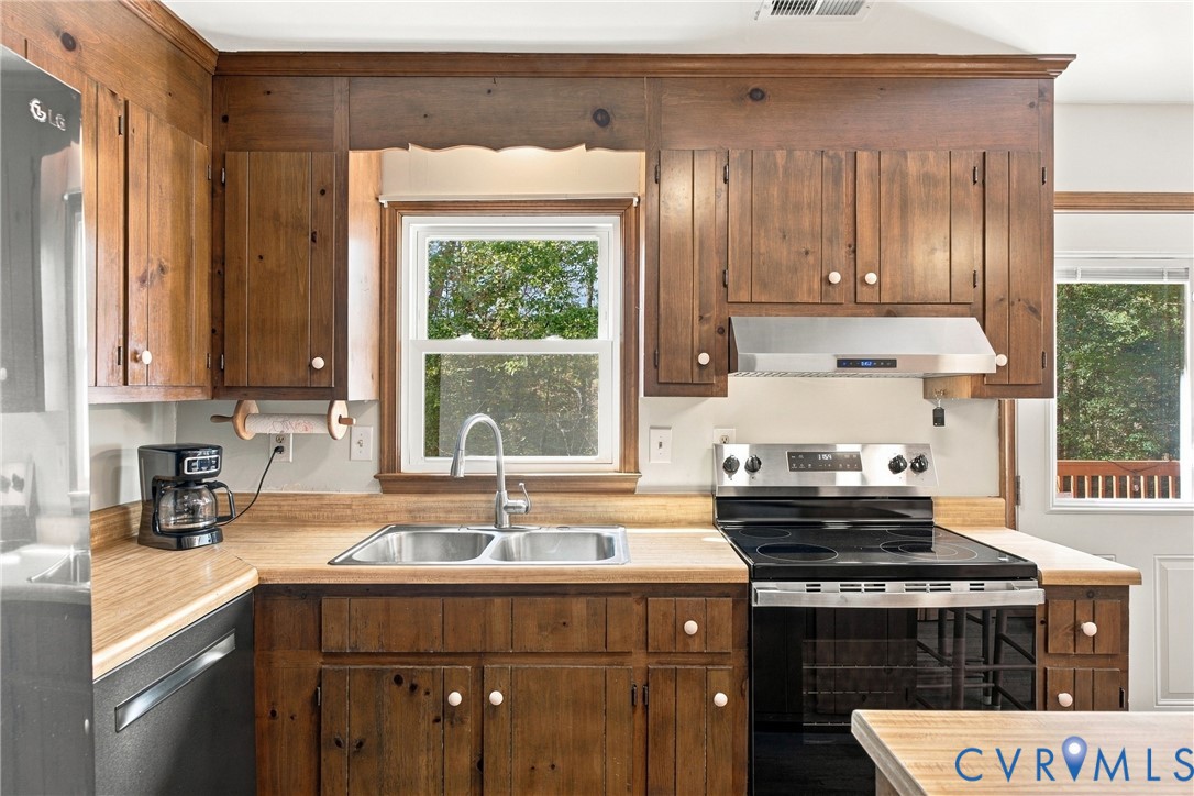 Kitchen featuring stained-wood cabinetry, stainless steel range with integrated vent hood, dual-basin stainless steel sink with gooseneck faucet, and laminate countertops