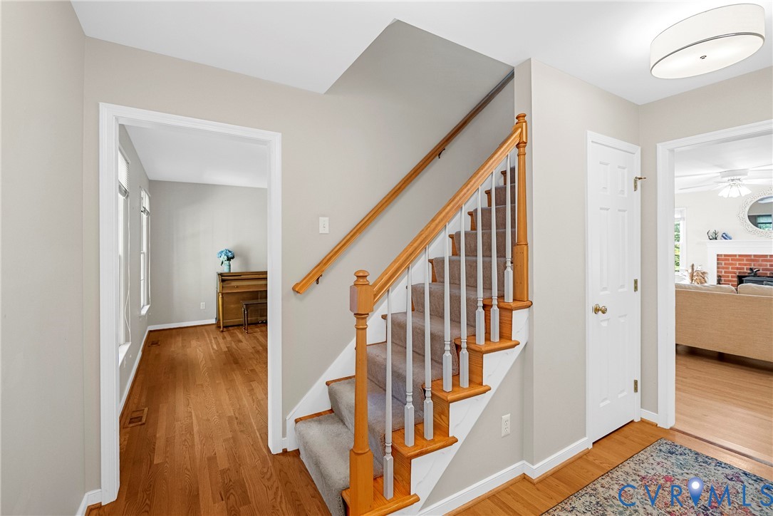 Staircase featuring a natural wood handrail, light-toned balusters, and carpeted treads, complemented by hardwood flooring and a ceiling-mounted drum light fixture