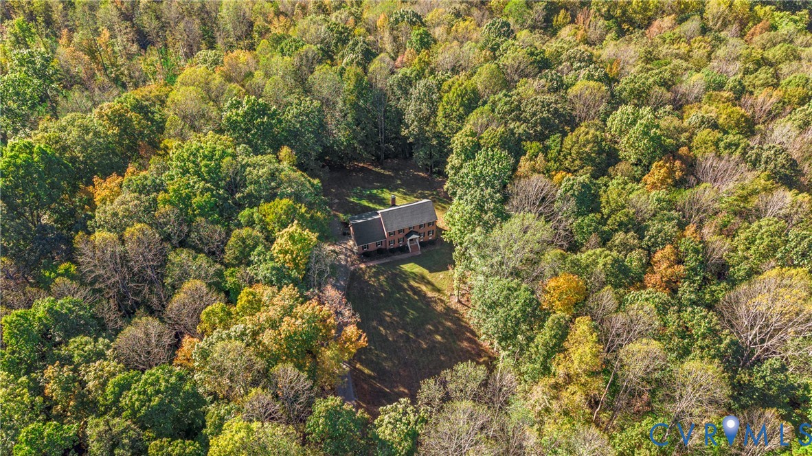 Two-story residential structure featuring a dark-toned shingled roof, set within a lot characterized by extensive mature tree coverage and private woodland
