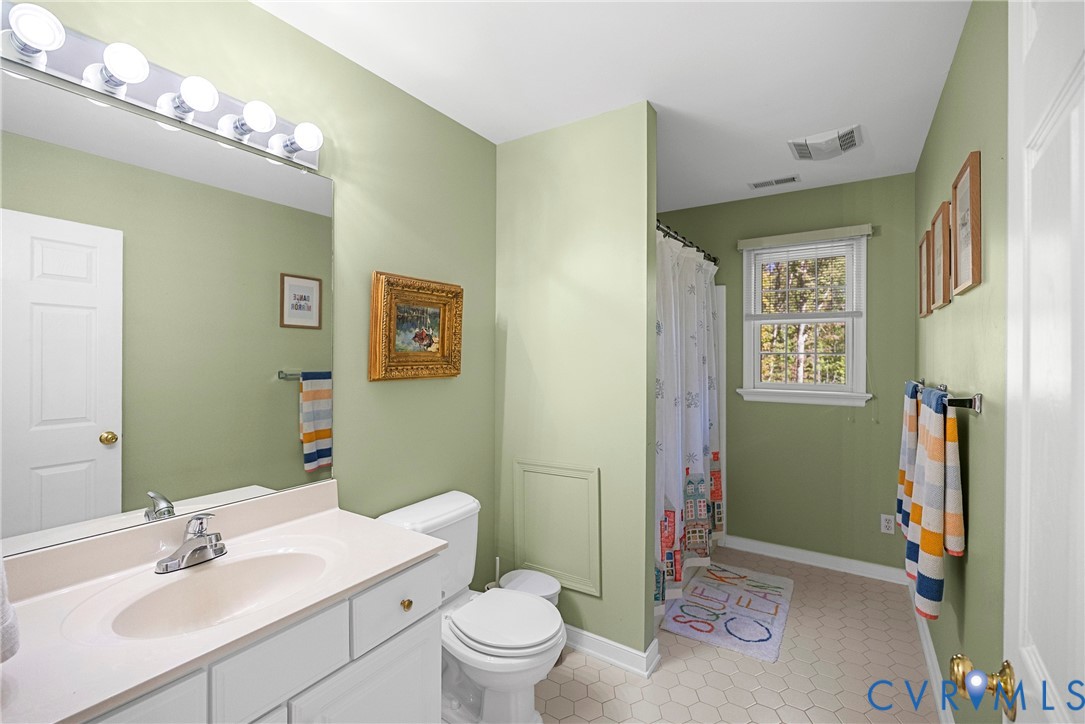 Bathroom featuring a white vanity with an integrated sink, a full-width vanity mirror, multi-bulb wall lighting, a window, and hexagon-patterned tile flooring