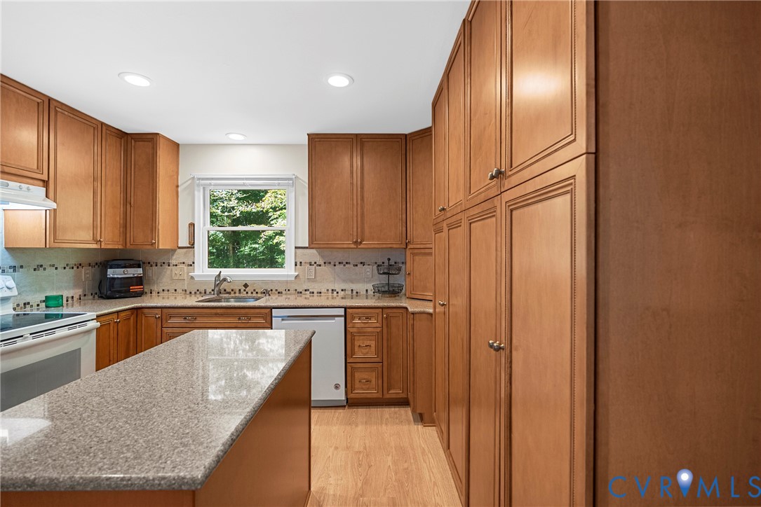 Kitchen featuring wood cabinetry, floor-to-ceiling pantry storage, stone-surface countertops, recessed lighting, and tile backsplash