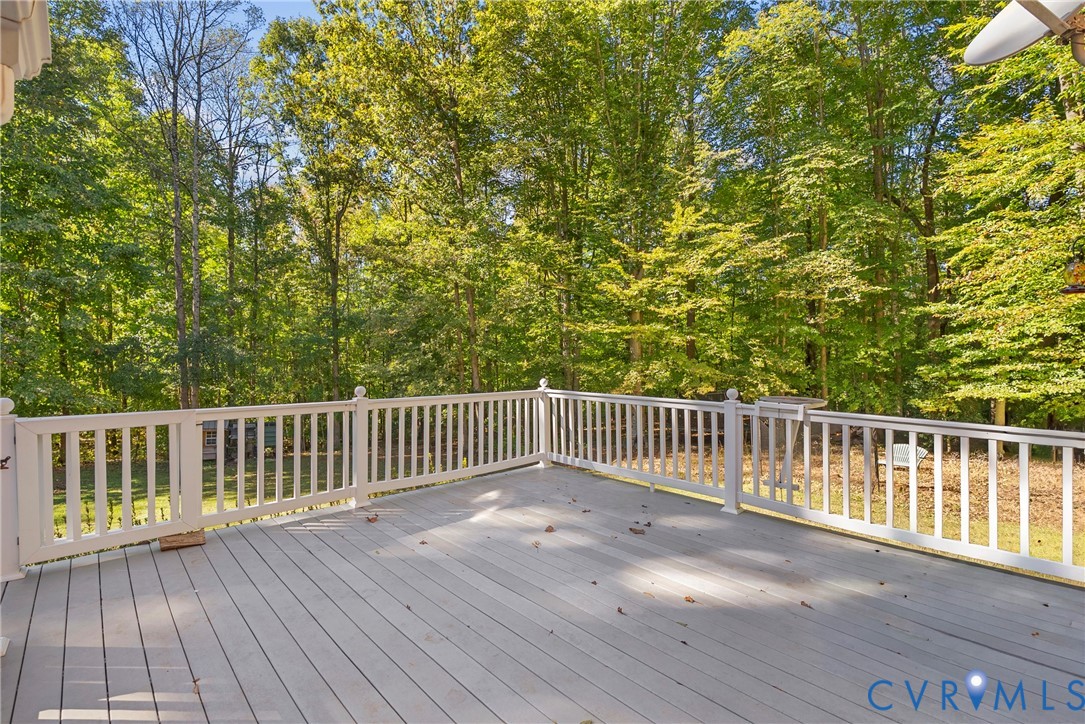 Elevated deck featuring gray composite decking, white picket-style railings, and a wooded backdrop
