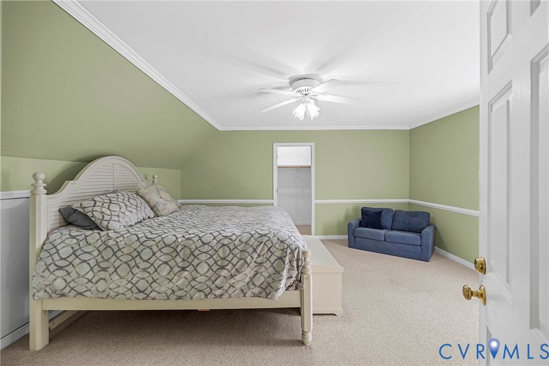 Sloped ceiling featuring crown molding, neutral carpeting, chair rail trim, and a ceiling-mounted light fixture with fan
