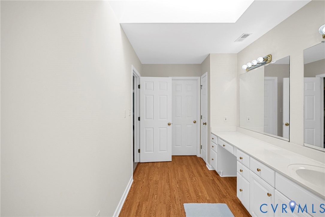 Long vanity with countertop and dual sinks, wood-finish flooring, skylight, and multi-panel doors