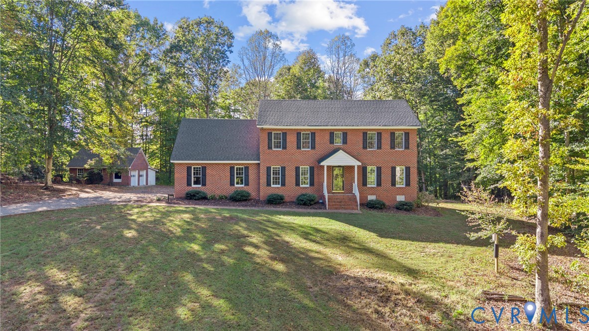 Two-story brick exterior featuring a shingled roof, dark window shutters, a covered front entryway, and a separate detached garage situated on a lot with mature trees
