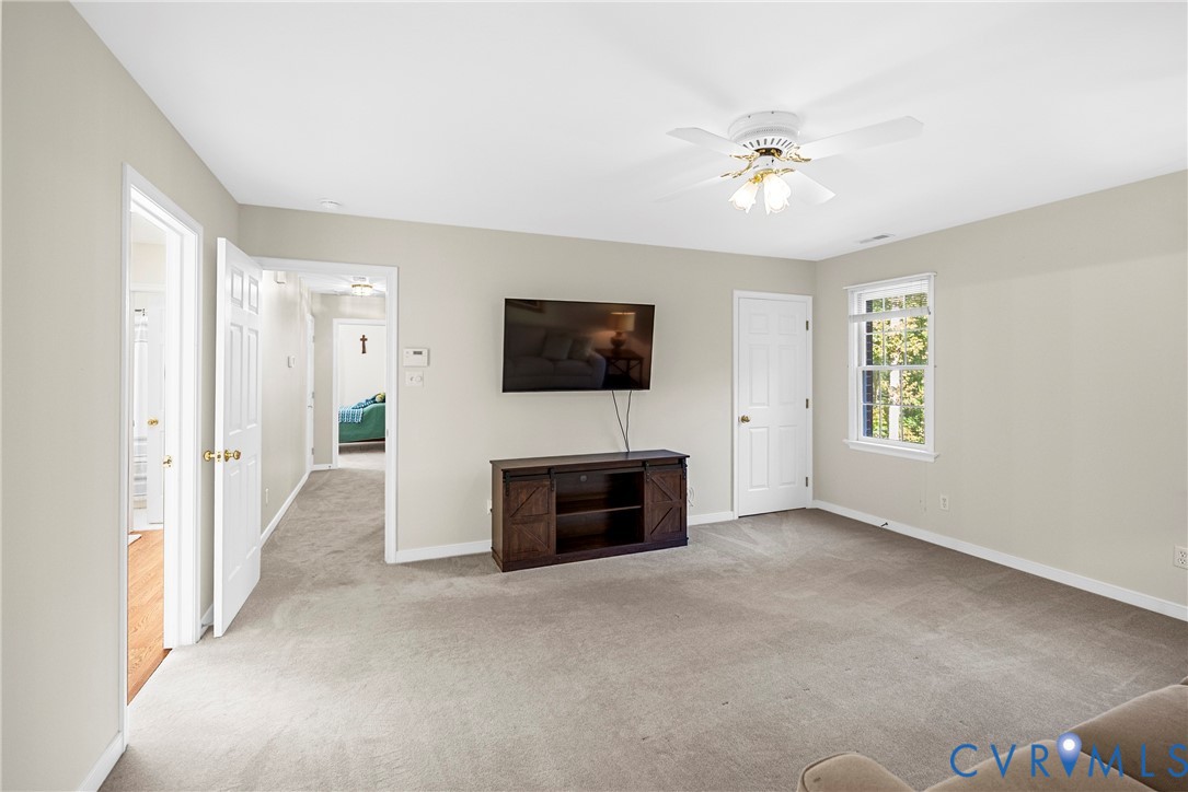 Neutral-toned interior featuring wall-to-wall carpeting, a multi-blade ceiling fan with integrated light fixture, and a single-hung window