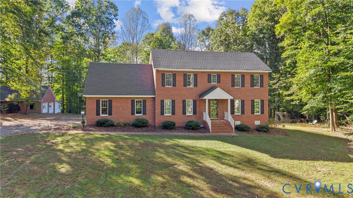 Two-story brick exterior featuring a shingled roof, dark shutters, a covered front entry with white railings, and a multi-car detached garage