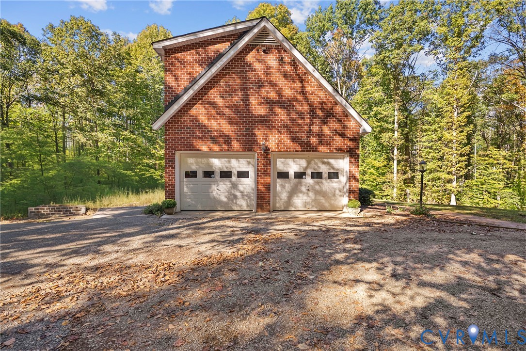 Detached two-car garage featuring a red brick exterior, a gabled roofline, and white overhead doors with rectangular window inserts