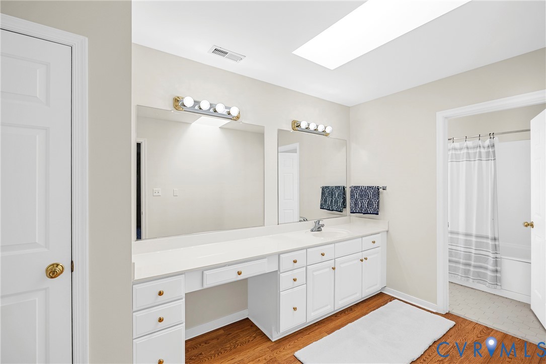 Dual-sink vanity with white cabinetry, light-toned countertop, skylight, and wood-finish flooring