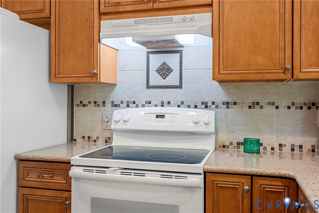 Kitchen featuring wood cabinetry, stone-finish countertops, tile backsplash with decorative inset, and a built-in range hood