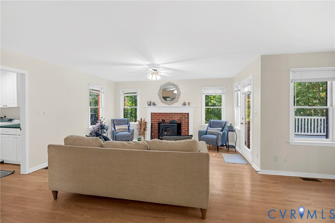 Living space featuring wood-finish flooring, brick fireplace with a wood-burning insert, mantel, multiple windows, and a ceiling fan