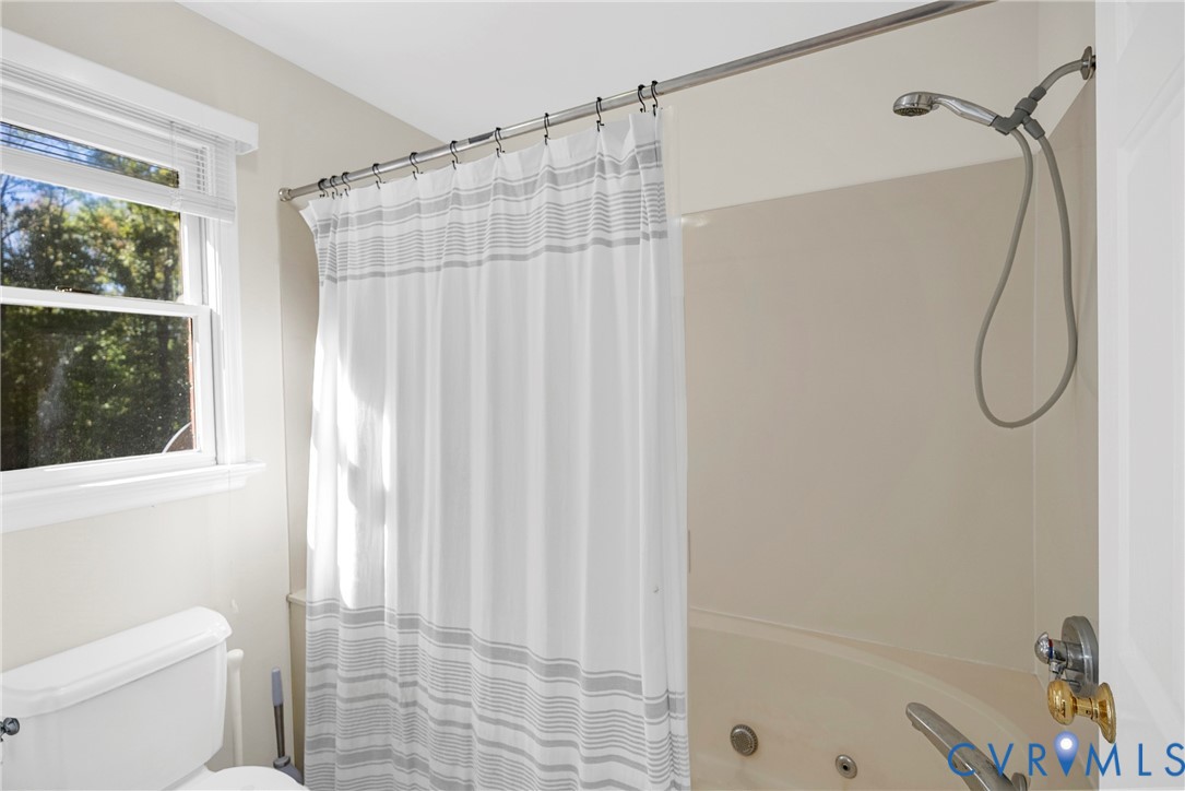 Bathroom featuring a jetted tub, a wall-mounted shower head, and a double-hung window