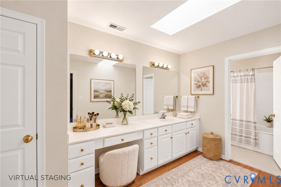 Double vanity with an integrated countertop, skylight, white shaker-style cabinetry, and polished hardware