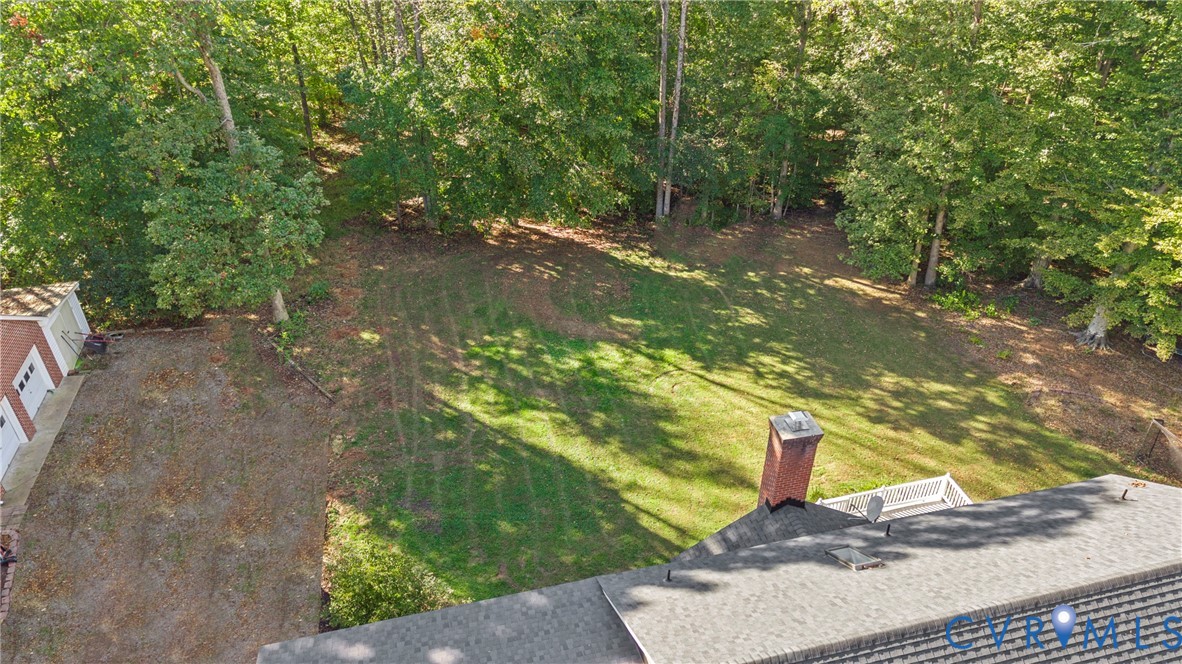 Expansive rear yard featuring mature trees, a brick chimney, an elevated deck, and a detached structure