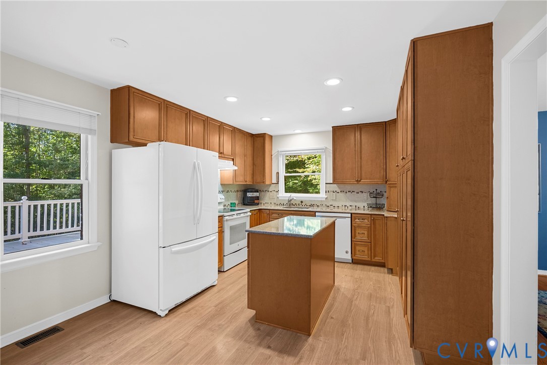 Kitchen featuring shaker-style wood cabinetry, center island, stone-finish countertops, tile backsplash, and wood-finish flooring