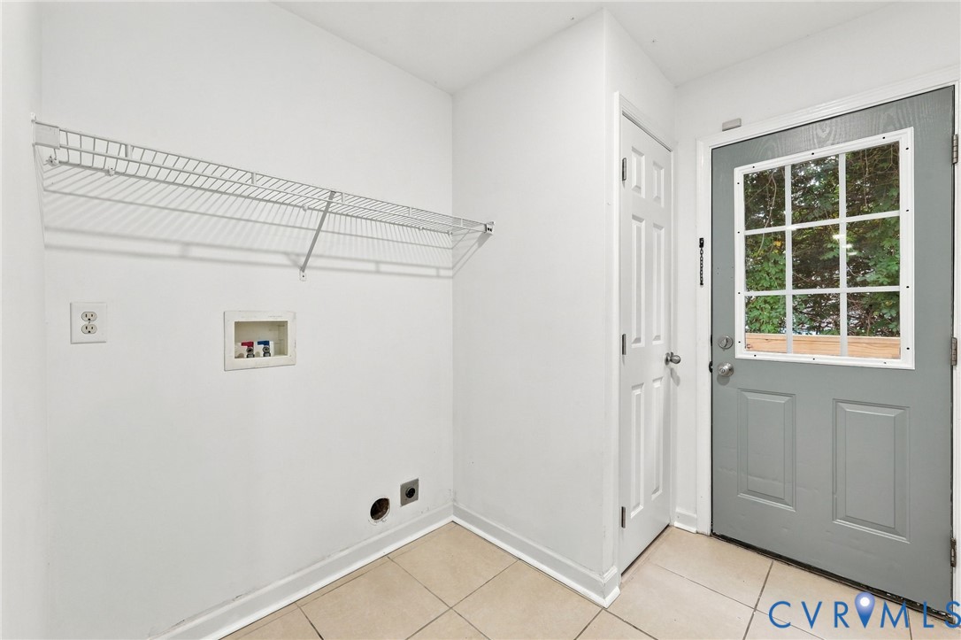 Utility area featuring ceramic tile flooring, a wall-mounted wire shelving unit, dedicated laundry hookups, a six-panel door, and a glass-paneled exterior door