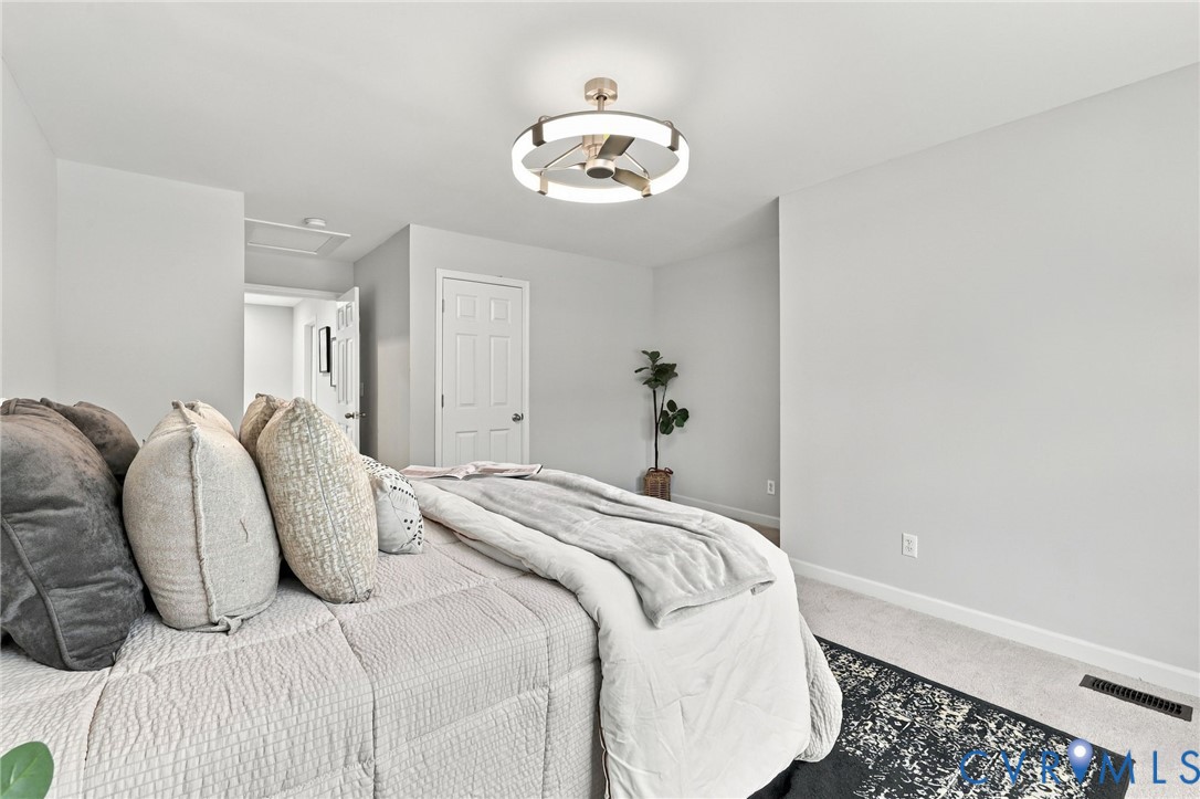 Modern circular flush-mount ceiling fan featuring a metallic finish and integrated ring lighting, complemented by neutral-toned wall-to-wall carpeting and a traditional six-panel interior door