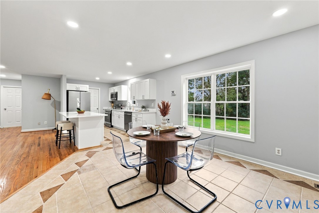 Kitchen featuring white cabinetry, an island with a light-toned countertop, wood-finish flooring, large-format tile flooring with decorative inlay, and recessed lighting