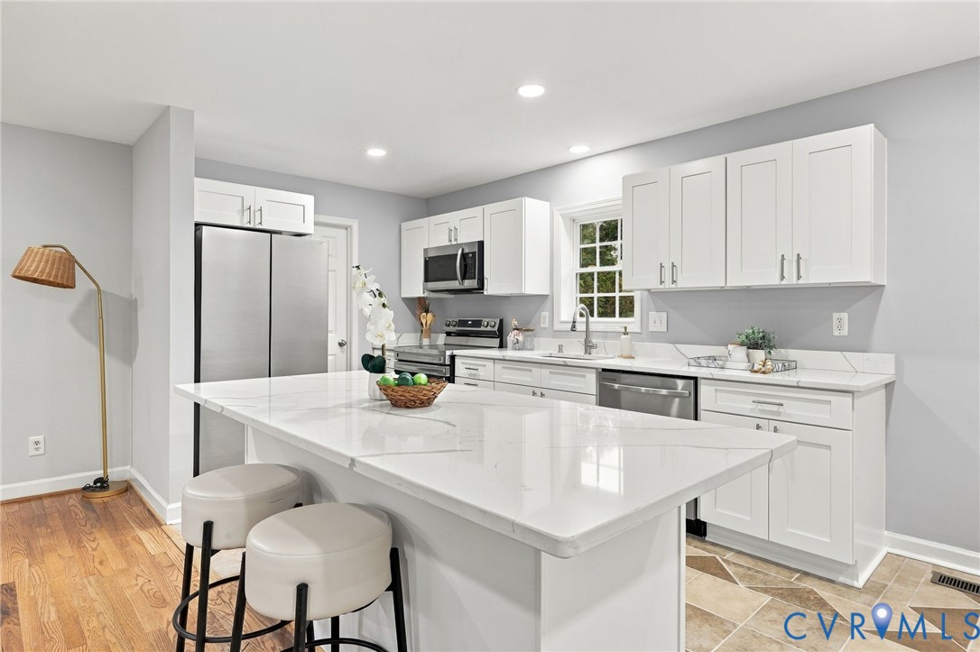 Kitchen featuring white shaker-style cabinetry, white countertops with subtle veining, stainless steel appliances, a center island, and wood-finish flooring Kitchen featuring white shaker-style cabinetry, white countertops with subtle veining, stainless steel appliances, a center island, and wood-finish flooring