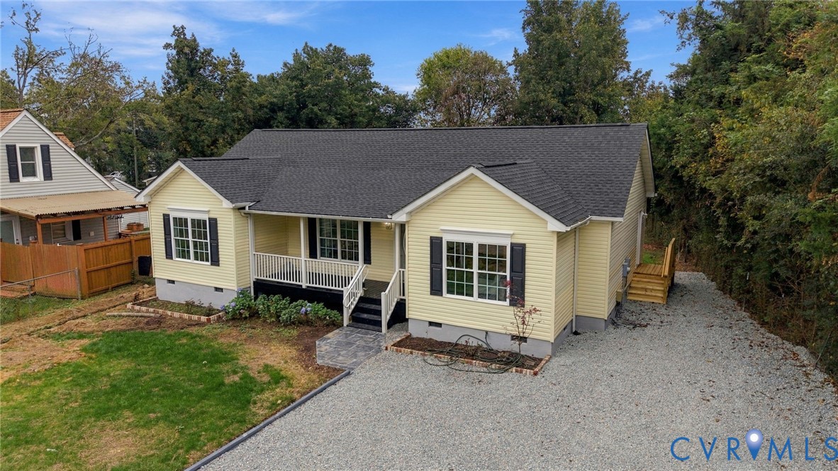 Exterior featuring pale yellow siding, dark shutters, a covered front porch with white railing, and a gravel driveway