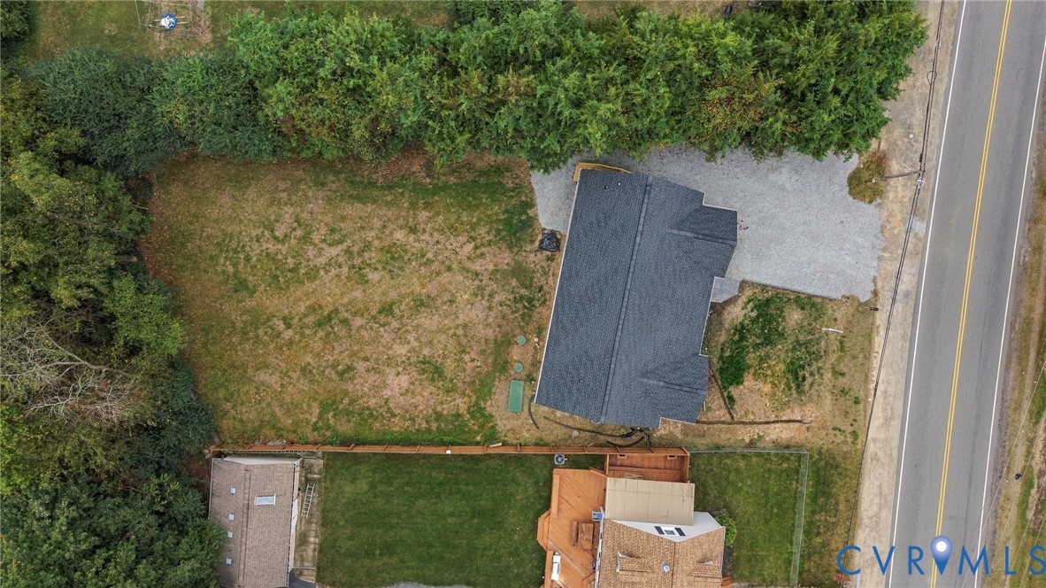 Aerial perspective featuring an expansive parcel of land, gravel driveway, mature perimeter tree lines, and a dedicated storage structure