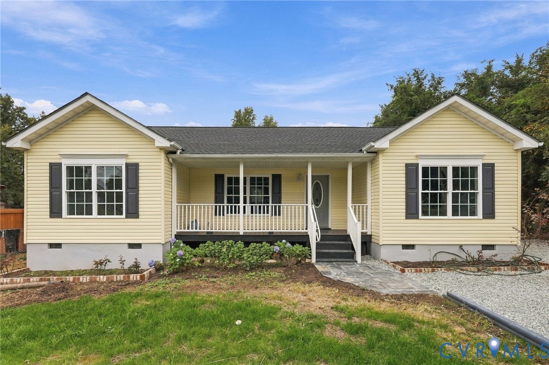 Single-story residence featuring pale yellow horizontal siding, a covered front porch with white railing, contrasting dark shutters, and a grey shingle roof Single-story residence featuring pale yellow horizontal siding, a covered front porch with white railing, contrasting dark shutters, and a grey shingle roof